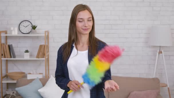 Primer plano retrato de alegre joven ama de casa sosteniendo colorido polvo cepillo y sonriendo a la cámara en casa — Vídeos de Stock