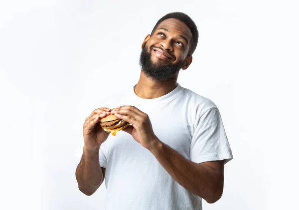 Feliz preto milenar cara segurando saboroso hambúrguer, fundo branco — Fotografia de Stock