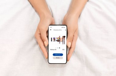 Ekranda çevrimiçi makyaj dükkanı olan kadın eller telefonu tutuyor.