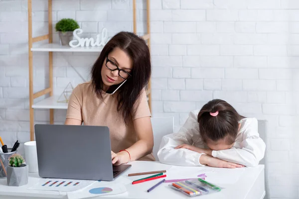 Busy mom working on laptop and talking on phone at home, lonely depressed child sitting nearby