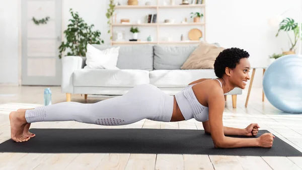 Heimtraining. Schwarze Frau trainiert auf Yogamatte, macht Ellbogenplanken-Pose, stärkt ihre Bauchmuskeln — Stockfoto