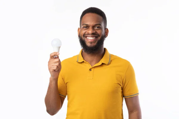 Happy Black Guy Showing Energy-Saving Lightbulb Standing Over White Background — Stock Photo, Image