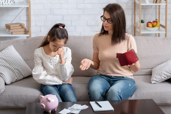 Upset mother and her daughter with empty wallet and heap of unpaid bills having financial problems at home