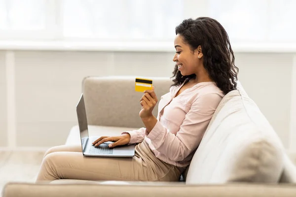 Mujer negra usando computadora y tarjeta de crédito en casa —  Fotos de Stock