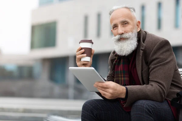 Handsome aged man holding coffee and using digital tablet