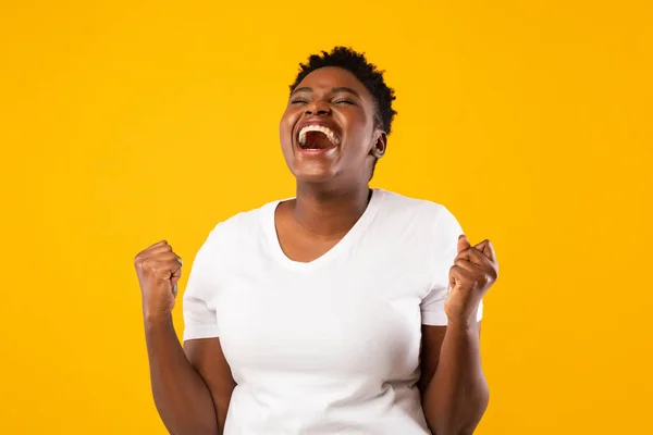 Örömteli fekete nő kiabálva rázó öklök pózol át sárga háttér — Stock Fotó