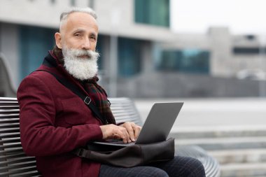 Modern büyükbaba bankta otururken dizüstü bilgisayar kullanıyor