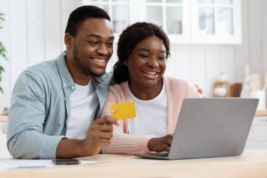 Mutfakta dizüstü bilgisayarı ve kredi kartı olan siyah çift online alışveriş yapıyor.