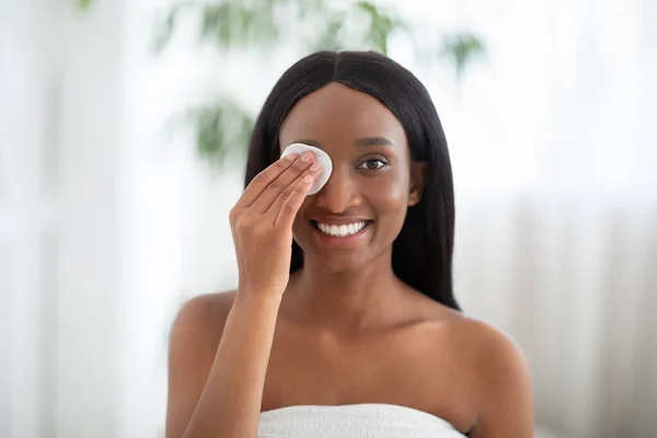 Senhora americana africana alegre limpa a pele com almofada de algodão e produtos cosméticos para limpeza adequada e profunda — Fotografia de Stock