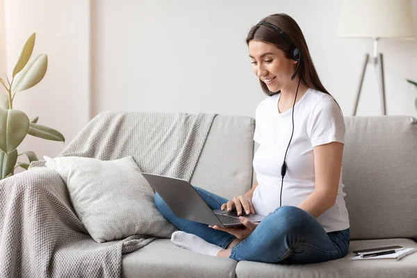 Έγκυος γυναίκα σε ακουστικά που χρησιμοποιούν φορητό υπολογιστή στο σπίτι, μελέτη ή εργασία σε απευθείας σύνδεση — Φωτογραφία Αρχείου