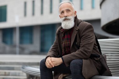 Düşünceli yaşlı bir adam işten sonra bankta dinleniyor.