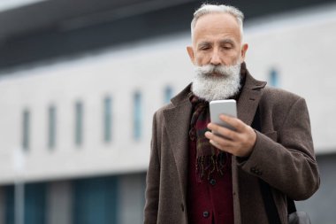 Zengin kıdemli adam modern akıllı telefonunu kontrol ediyor.