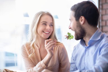 Sevecen genç bir çift kahve içip birbirlerini taze sebze salatasıyla besliyorlar.