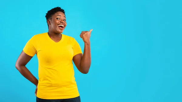 Túlsúlyos fekete nő mutatva hüvelykujj félre a kék háttér, panoráma — Stock Fotó