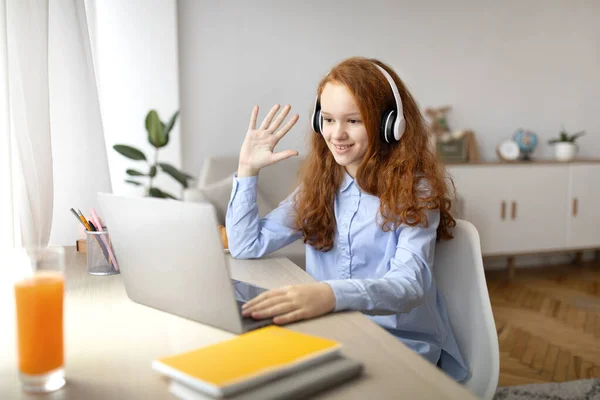Girl sitting at desk using computer and waving to webcam — Stock Photo, Image