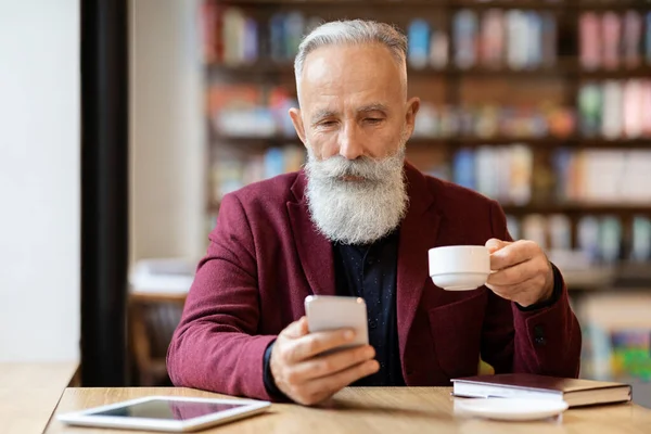 Hombre mayor de pelo gris bebiendo café y usando el teléfono — Foto de Stock