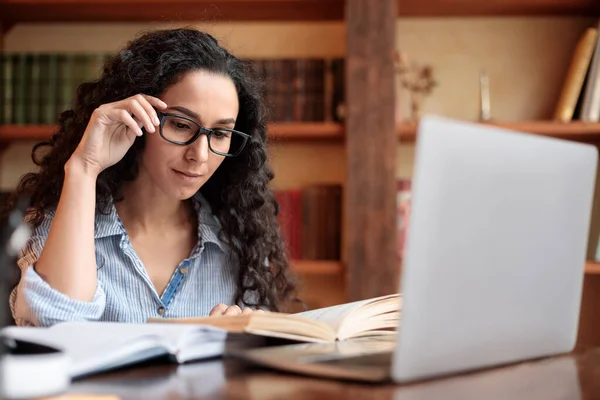 Jongedame leesboek zittend aan bureau aanraken bril — Stockfoto