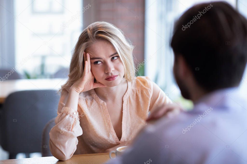Young Caucasian woman disinterested in blind date, feeling bored with conversation at city cafe
