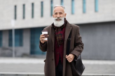 Caddede yürüyen, kahve içen mutlu yaşlı adam.