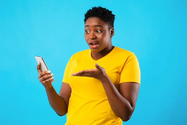 불만을 품은 흑인 여자가 푸른 배경 위에서 스마트폰을 들고 문제를 겪고 있다 — 스톡 사진