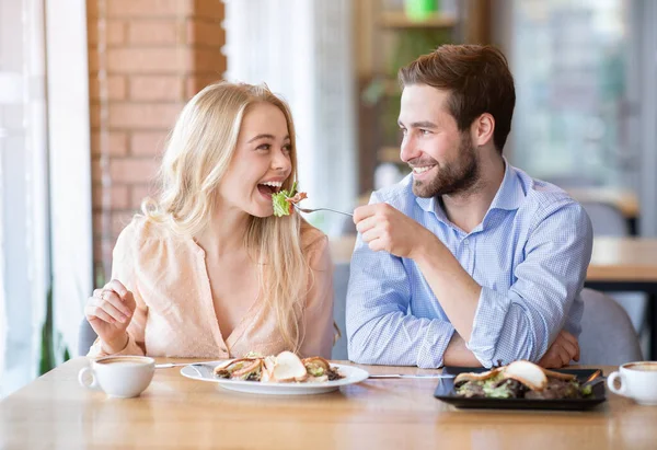 Gioiosa giovane coppia che pranza insieme alla caffetteria, uomo millenario che dà insalata alla sua ragazza — Foto Stock