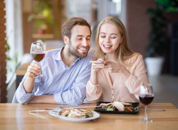 Sevecen bir milenyum çifti restoranda lezzetli yemek ve şarabın fotoğrafını çekiyor. — Stok fotoğraf