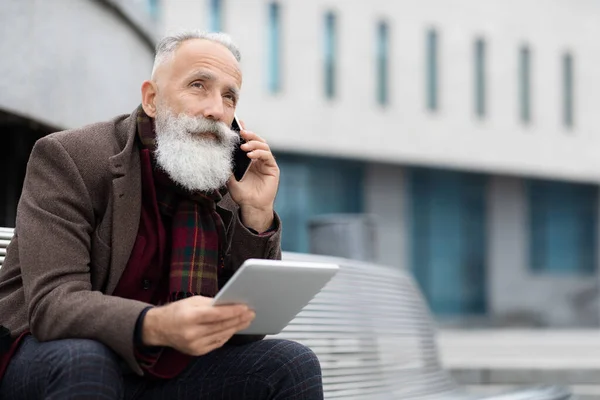 Elinde dijital tablet olan ve telefonla konuşan yaşlı bir adam. — Stok fotoğraf