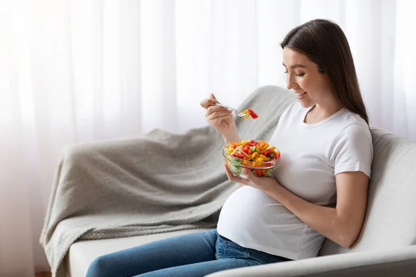 ビタミン食品。カウチに座りながら野菜サラダを食べる幸せな妊婦 — ストック写真