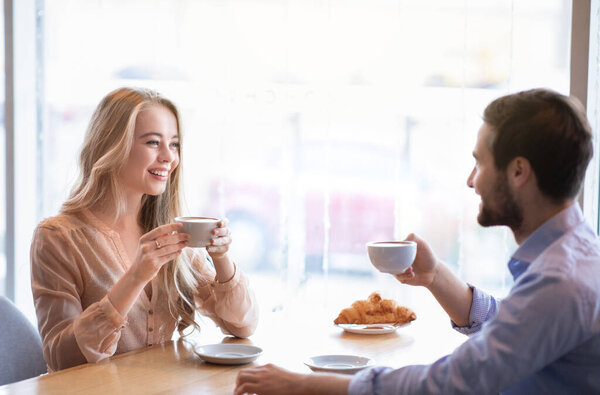 Portrait of affectionate couple sitting at table in city cafe, drinking aromatic coffee, enjoying each others company