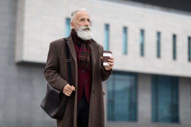 Yakışıklı yaşlı adam ofise gidiyor, kahve içiyor.