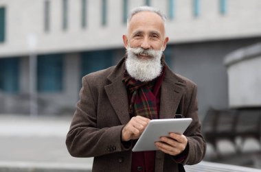 Sokakta yürüyen dijital tabletli gülümseyen yaşlı adam.