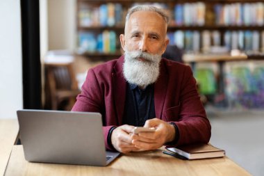 Kafede akıllı telefon kullanan zengin yaşlı bir adam.