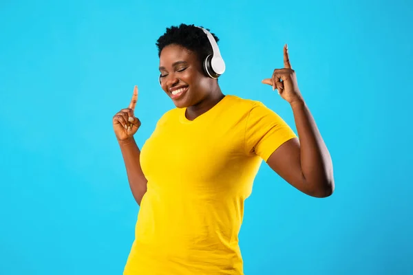 Χαρούμενος συν-μέγεθος Αφρικής γυναίκα που χορεύει ακούγοντας μουσική, μπλε φόντο — Φωτογραφία Αρχείου