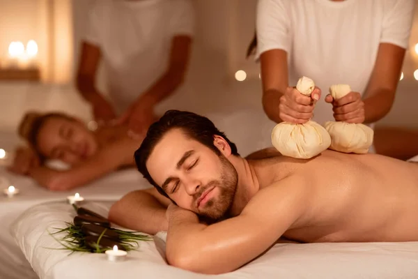 Casal relaxante durante a massagem de ervas nas costas com sacos aromáticos no interior — Fotografia de Stock