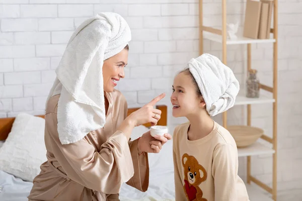 Sonriente madre aplicando crema en su cara de hijas lindas, organizando salón de belleza en casa, teniendo día de spa juntos —  Fotos de Stock
