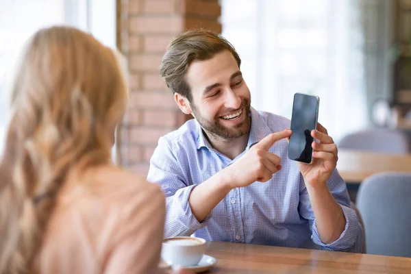 Uomo attraente che mostra il suo smartphone fidanzata con schermo vuoto in mensa, mockup per il design del sito web o app mobile — Foto Stock