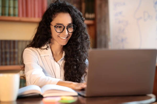 Kvinna i glasögon sitter vid skrivbordet och använder laptop — Stockfoto