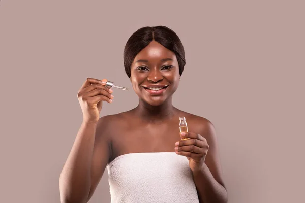 Nutrição da pele. Garrafa de segurando bela senhora afro-americana com soro facial hidratante — Fotografia de Stock