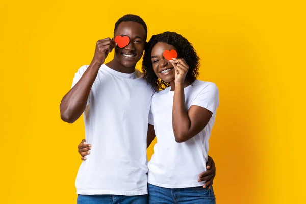 Amantes negros abraçando e segurando corações vermelhos no amarelo — Fotografia de Stock