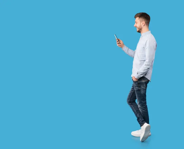 Pria ceria Dengan Ponsel SMS Selama Latar Belakang Biru, Panjang Penuh — Stok Foto