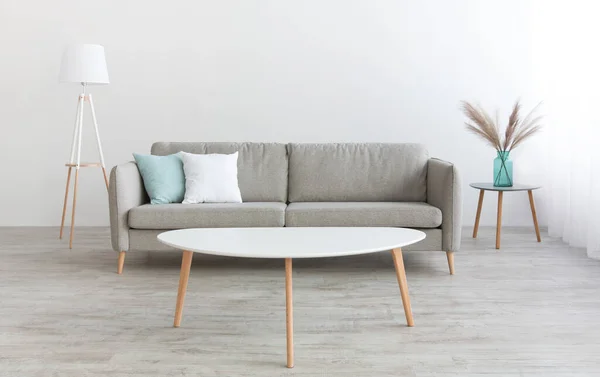 Table blanche, canapé moderne avec oreillers blancs et bleus, lampe et vase avec plantes sèches à la maison avec murs gris — Photo