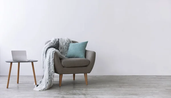 Sillón moderno con almohada azul y suave cuadros, junto a una pequeña mesa con portátil en el interior escandinavo —  Fotos de Stock