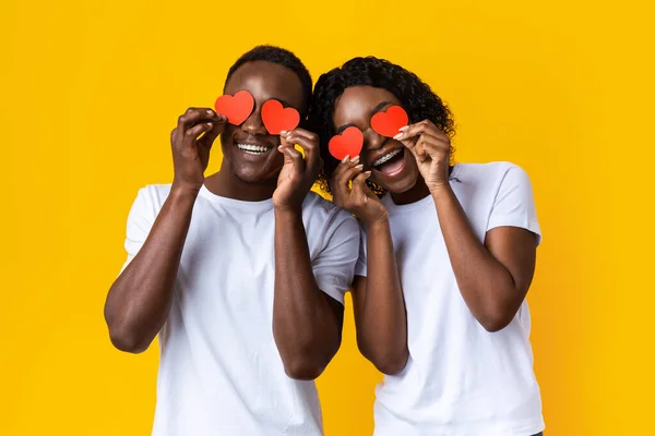 Unga svarta par som håller röd kärlek hjärtan över ögonen — Stockfoto