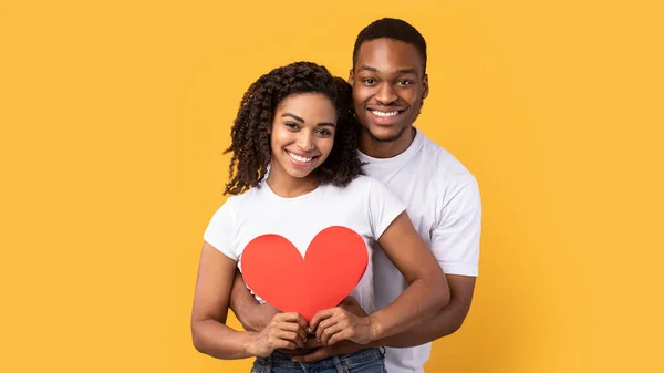 Pareja africana cariñosa abrazando el corazón sobre fondo amarillo, Panorama — Foto de Stock