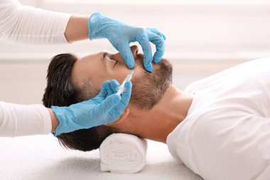 Klinikte güzellik iğnesi yaptıran sakallı adamın yan görüntüsü.