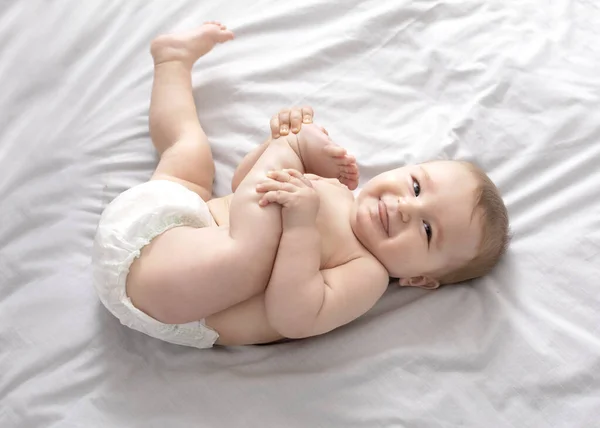 Güzel beyaz bebek yatakta uzanıyor, ayaklarla oynuyor. — Stok fotoğraf