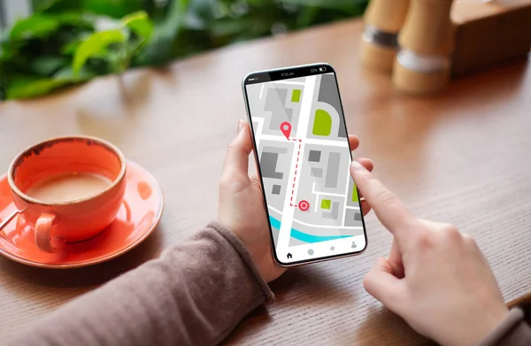 Unrecognizable woman using online maps application on smartphone while sitting in cafe