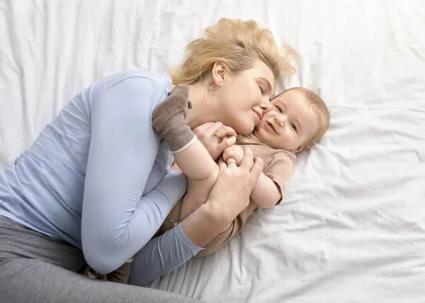 Älskade mor smeker sin lilla pojke i sängen — Stockfoto