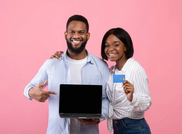 Siyah adam boş dizüstü bilgisayarı işaret ediyor, kız arkadaşı pembe arka planda kredi kartı tutuyor, tasarım için model. — Stok fotoğraf