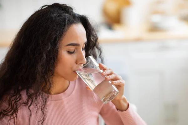 Liquido sano. Bella donna bruna che beve acqua minerale dal vetro in cucina — Foto Stock